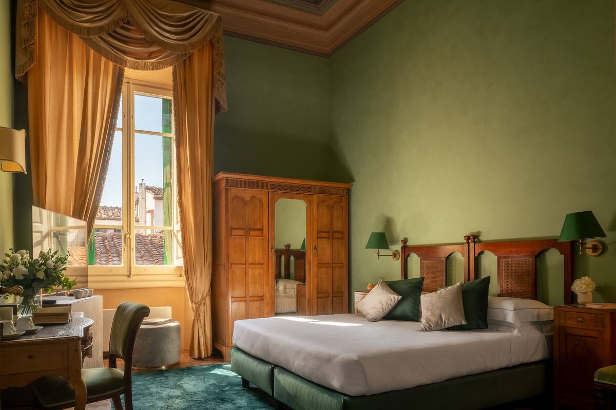 Une chambre à coucher comprenant un lit, un bureau, une chaise, une armoire et une fenêtre avec des rideaux.