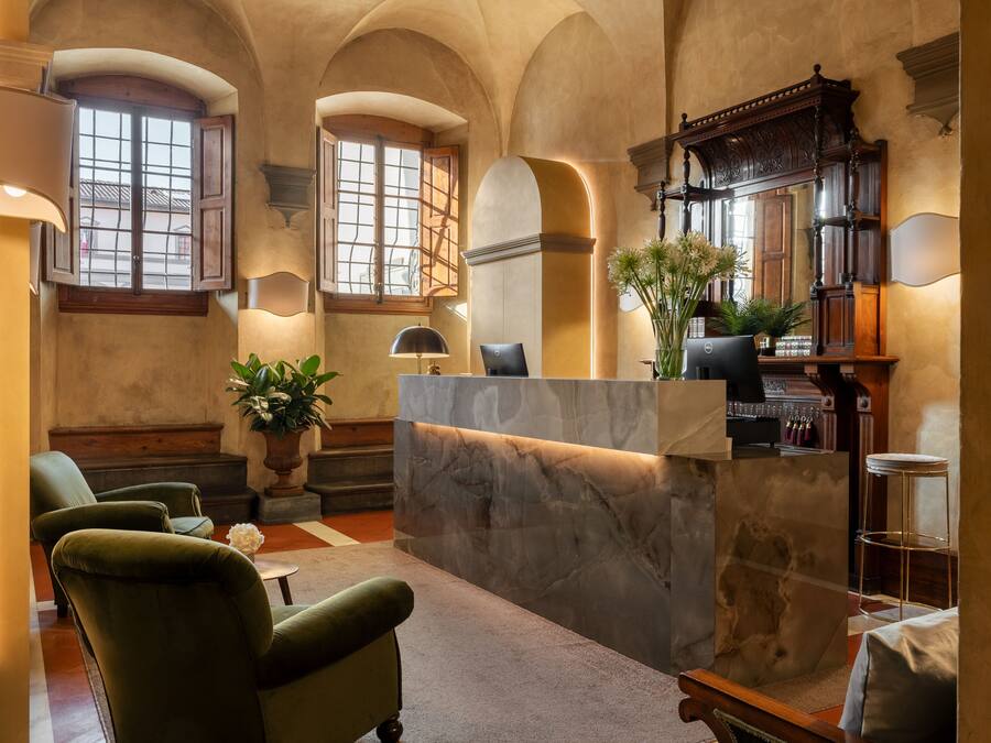 A lobby with a marble reception desk, green upholstered chairs, a potted plant, and a wooden bench.
