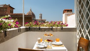 Un balcon avec une table dressée pour le petit-déjeuner, offrant une vue sur un paysage urbain avec des bâtiments historiques et un ciel dégagé.
