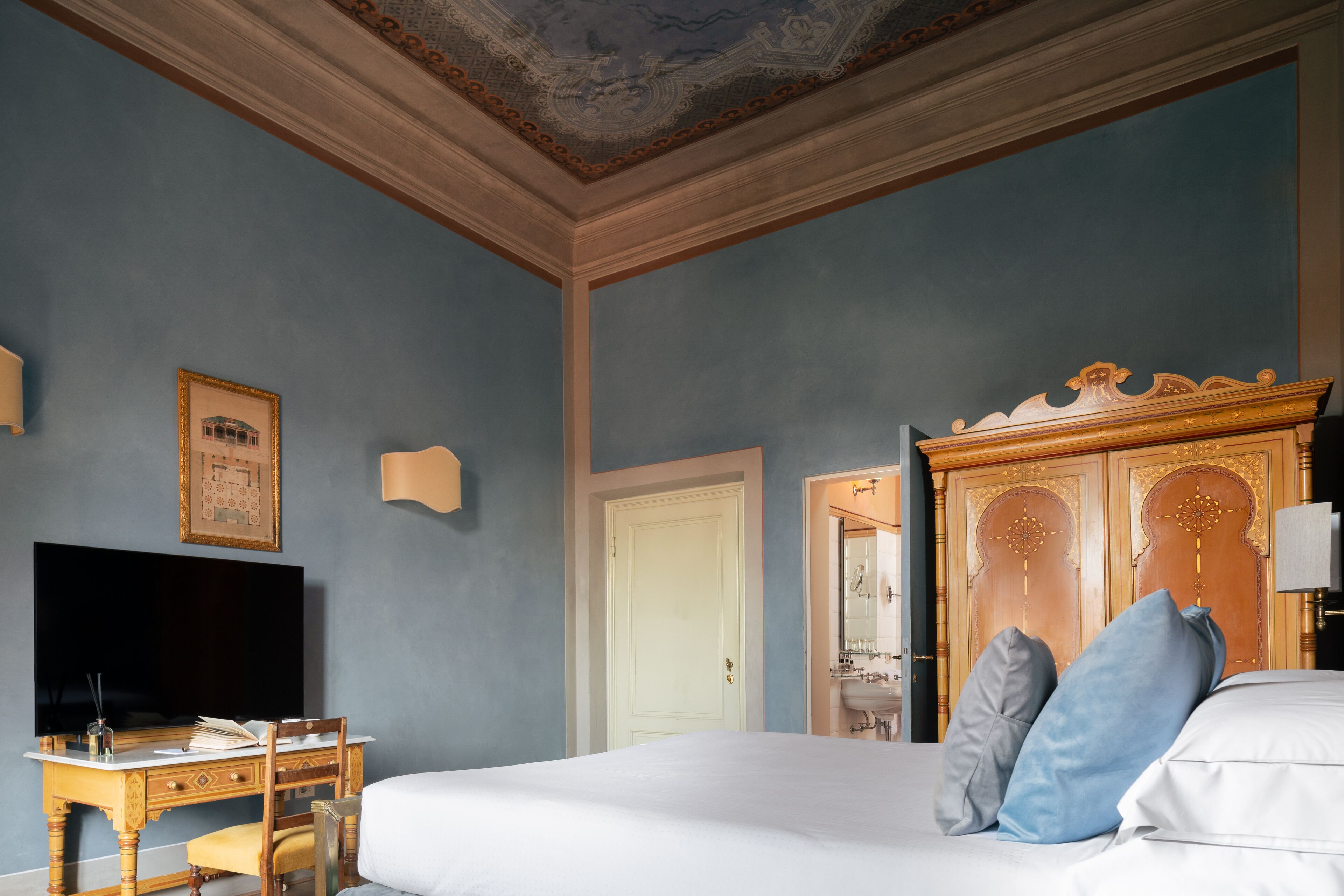 A bedroom with a large bed, a desk with a TV, and a wardrobe.