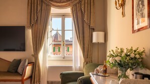 Une pièce comprenant un canapé, un fauteuil vert, une table avec un vase de fleurs, une lampe et une vue sur un bâtiment à l’extérieur.