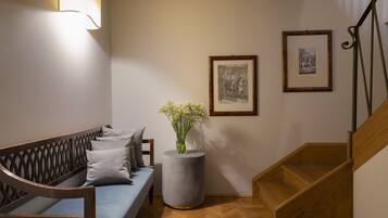 A modern living room with a wooden bench, a grey sofa, a round side table with a vase of flowers, and a staircase with wooden railings.