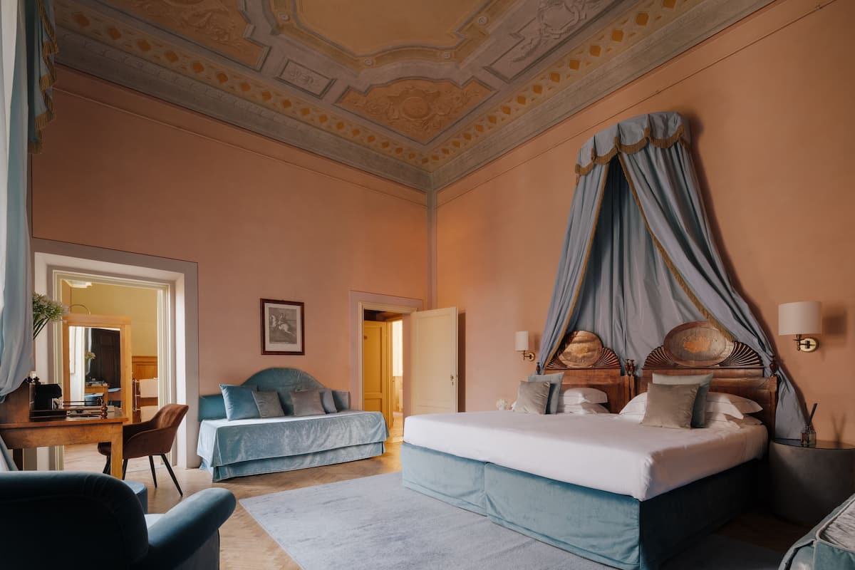 Une chambre avec un grand lit, un plus petit lit, un bureau et une chaise. On y trouve également un miroir, une lampe et une fenêtre.