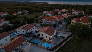 A residential area with houses featuring red-tiled roofs, a swimming pool, and a view of the sea at sunset. - Three bedroom villa with pool (Malinska)