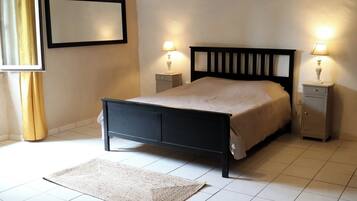 Une chambre à coucher avec un cadre de lit noir, une couvre-lit beige, deux tables de chevet avec des lampes, un tapis et un tableau encadré au mur.