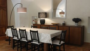 A dining area with a table set for four, a large mirror, a floor lamp, and a cabinet with decorative items.
