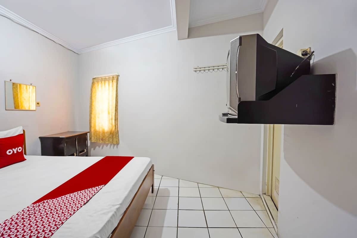 A hotel room with a bed, a TV mounted on the wall, a small table, and a window with curtains.