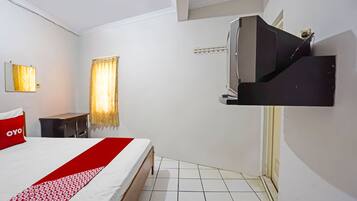 A hotel room with a bed, a TV mounted on the wall, a small table, and a window with curtains.
