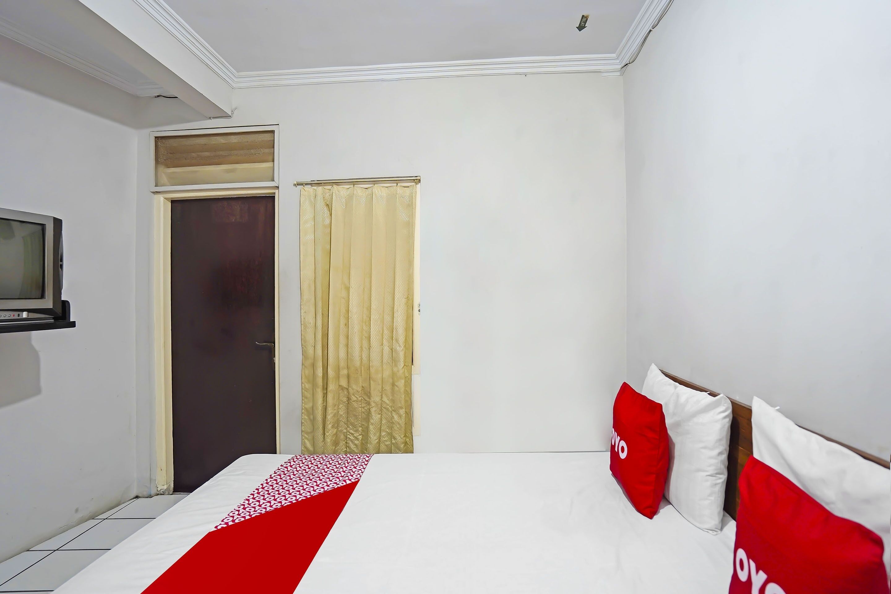 Una habitación de hotel con una cama, televisor, puerta y cortina.