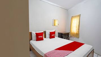 Une chambre d’hôtel avec un lit, deux oreillers rouges, une table de chevet, une lampe et une fenêtre avec des rideaux.