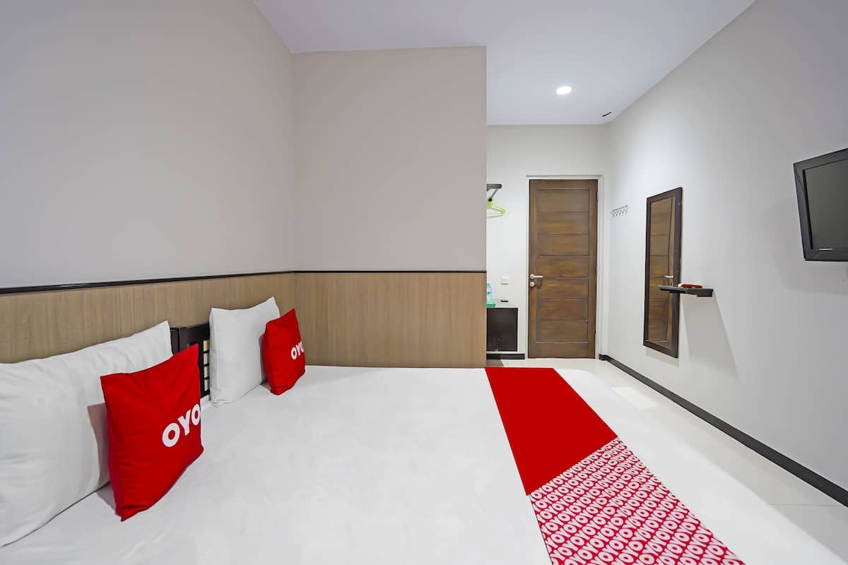 A hotel room with a bed, red and white pillows, a wooden door, and a TV mounted on the wall.