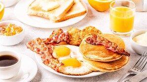 En frukosttallrik med ägg, bacon, rostat bröd och apelsinjuice.