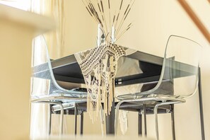 A modern dining area with clear glass tables and chairs, a decorative macrame centerpiece, and a neutral-toned wall. - Angel Luxury Apartment in Kriopigi (Kassandra)