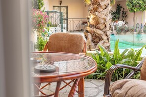 A wicker chair and table set on a patio with a stone floor, surrounded by greenery and a pool. - Angel Luxury Apartment in Kriopigi (Kassandra)
