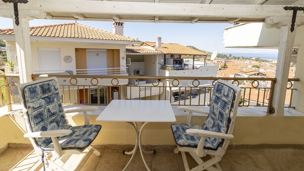 A balcony with two chairs and a table, overlooking a residential area with houses and a clear sky. - Sea View Maisonette in Pefkochori (Kassandra)