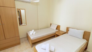 A hotel room with two single beds, a wooden wardrobe, a mirror, and an air conditioning unit. - Sea View Maisonette in Pefkochori (Kassandra)