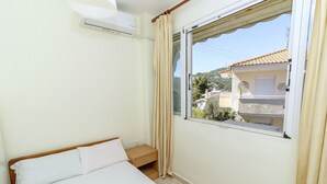 A bedroom with a bed, a nightstand, a window with curtains, and an air conditioning unit. - Sea View Maisonette in Pefkochori (Kassandra)
