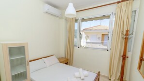 A bedroom with a bed, a wardrobe, a bedside table, a hanging lamp, and a window with curtains. - Sea View Maisonette in Pefkochori (Kassandra)