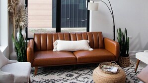 Ein modernes Wohnzimmer mit einem braunen Ledersofa, einem weißen Sessel, einem gemusterten Teppich und einer hohen Stehlampe.