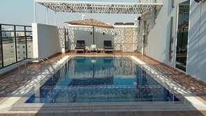 Una piscina en la azotea con sombrilla, sillas de piscina y vistas a la ciudad.