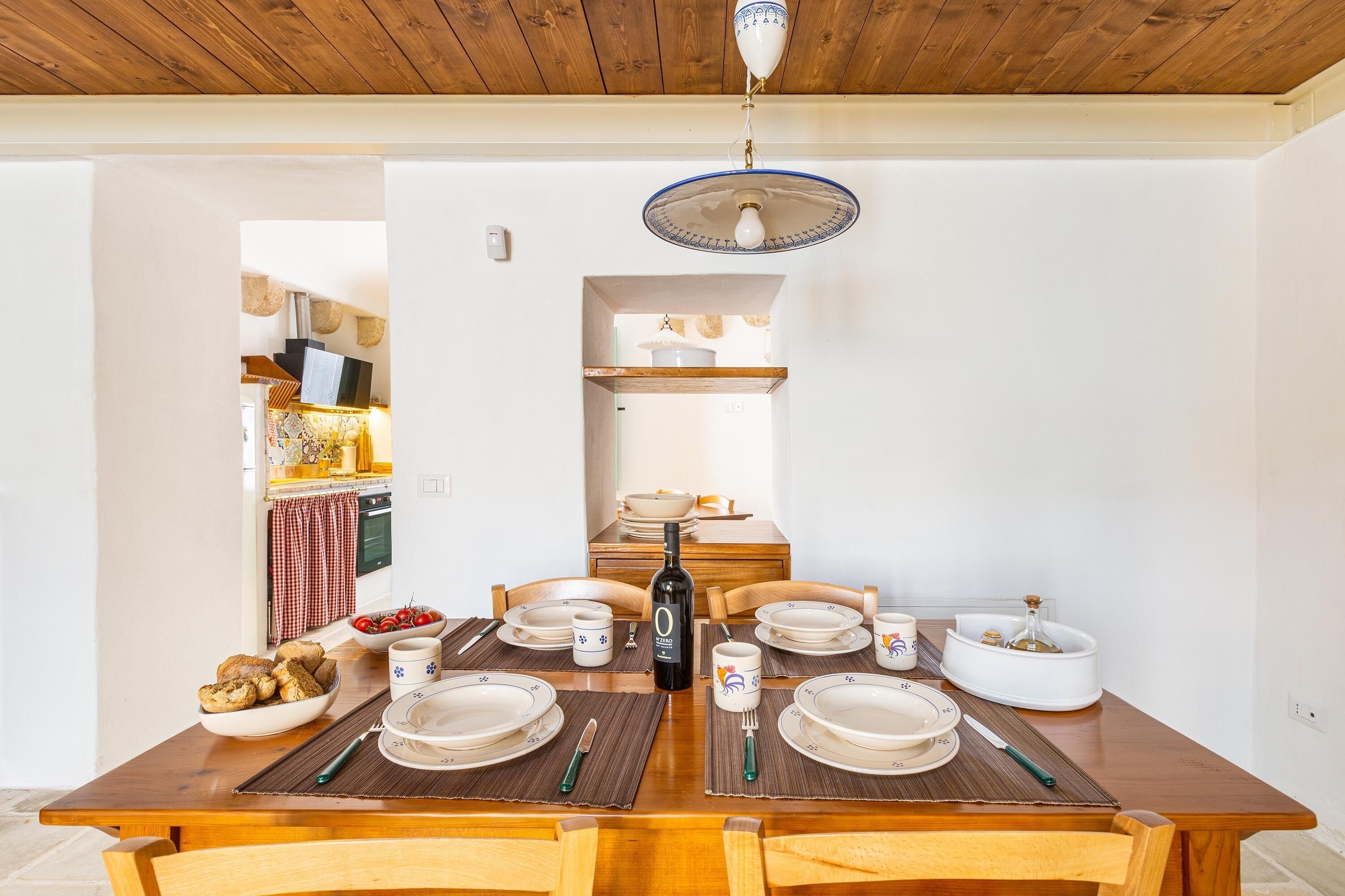 A dining area with a wooden table set for four, including plates, cutlery, and a bottle of wine.