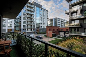 A modern apartment building with multiple balconies, a courtyard, and a view of a street with parked cars. - RentPlanet Kępa Mieszczańska (Wroclaw)