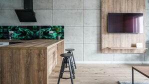 Una cucina moderna con isola in legno, sgabelli neri, TV a incasso e una schienale verde e ricco di vegetazione.