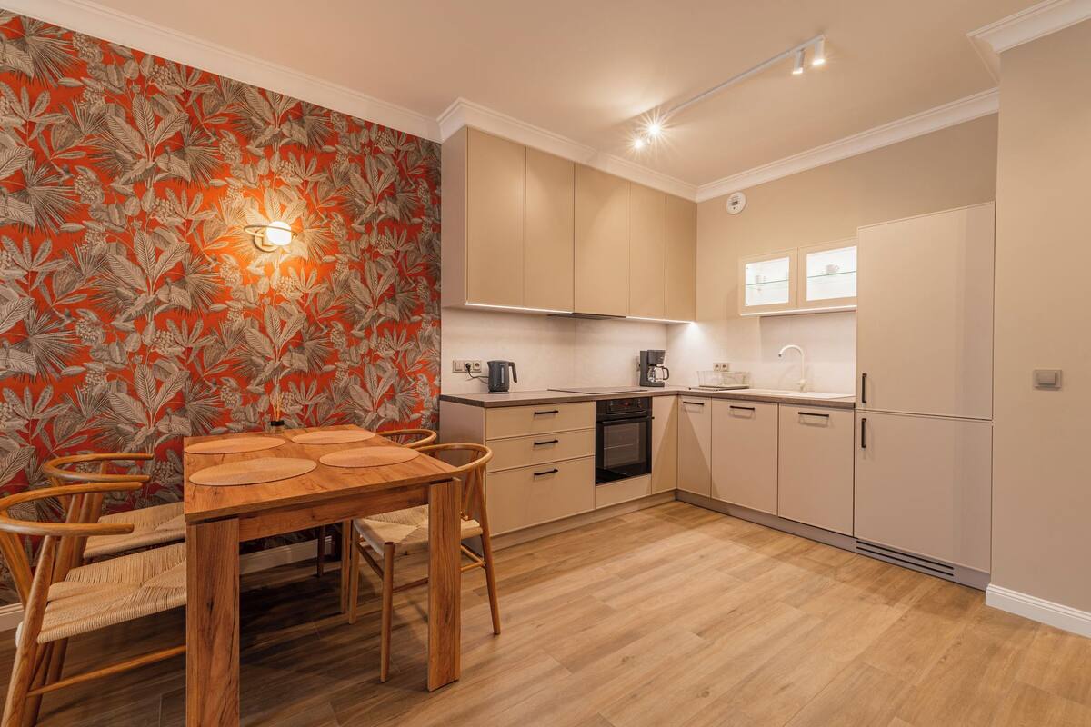 A modern kitchen with wooden cabinets, a dining table with chairs, and a patterned wallpaper.