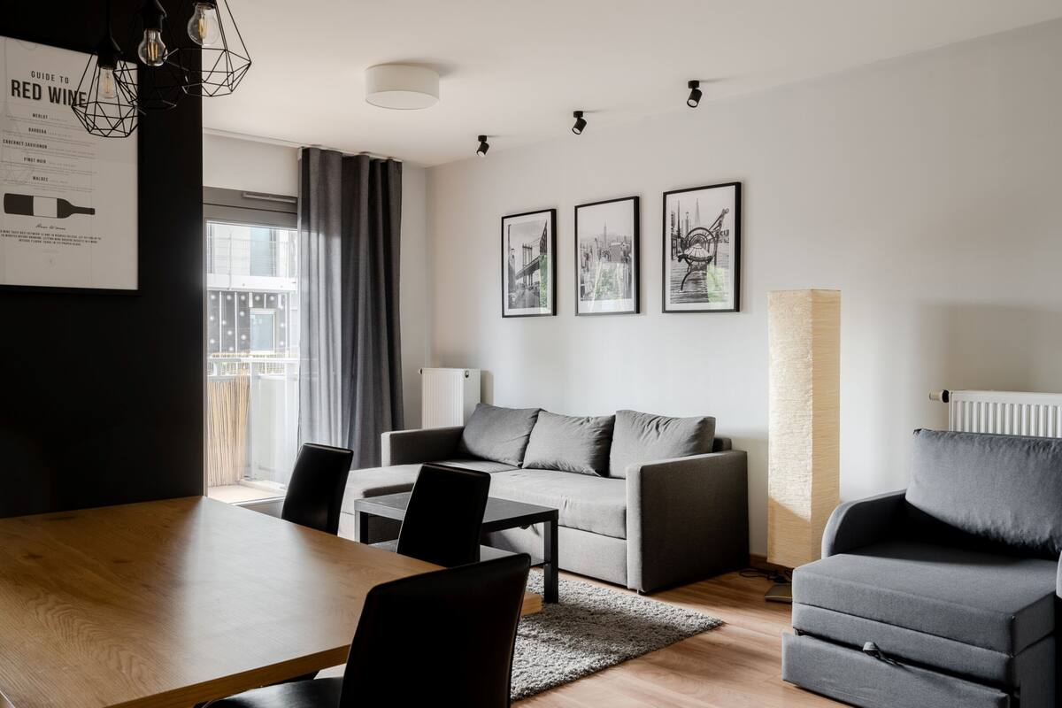 A modern living room with a sofa, a dining table with chairs, and a large window with curtains.
