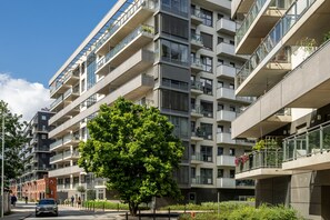 A multi-story residential building with balconies, a tree in the foreground, and a clear sky. - RentPlanet Kępa Mieszczańska (Wroclaw)