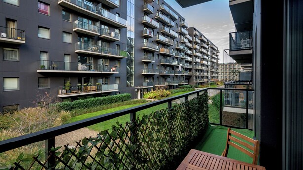 Un moderno edificio condominiale con balconi, un prato verde e un tavolo di legno su un balcone.