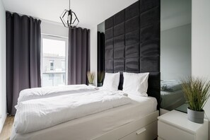 A modern bedroom with a large bed, a headboard, and a bedside table with a plant. - RentPlanet Kępa Mieszczańska (Wroclaw)