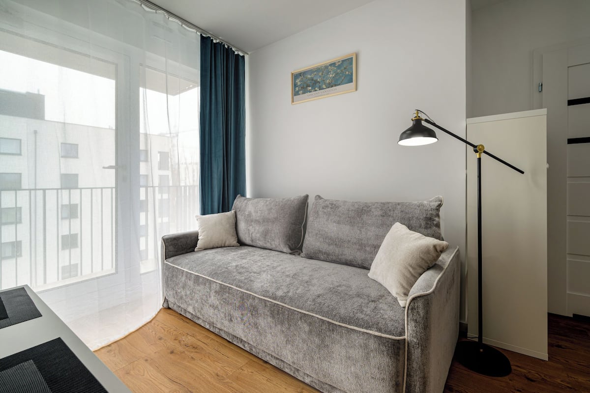 A grey sofa with pillows, a floor lamp, and a painting on the wall.