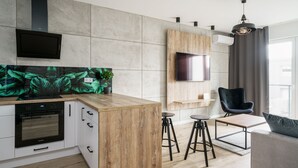 Una cucina moderna con forno a incasso e isola in legno. C'è una TV montata a parete e una poltrona nella zona living.
