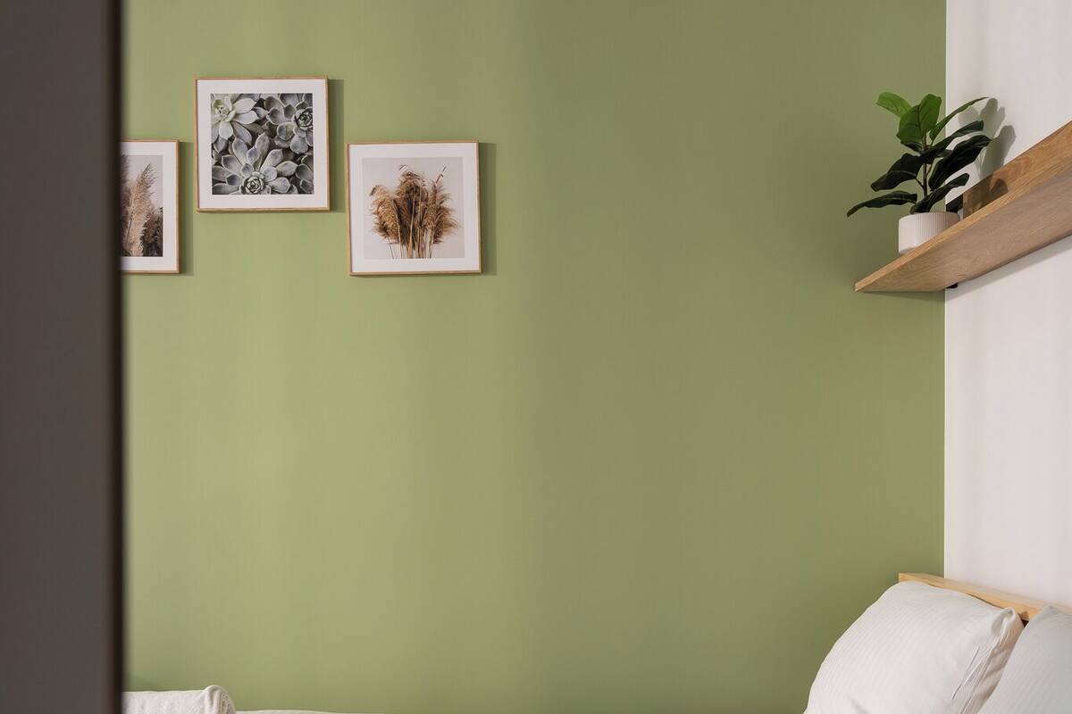 A bedroom with a green wall, a bed with white bedding, and three framed pictures on the wall.