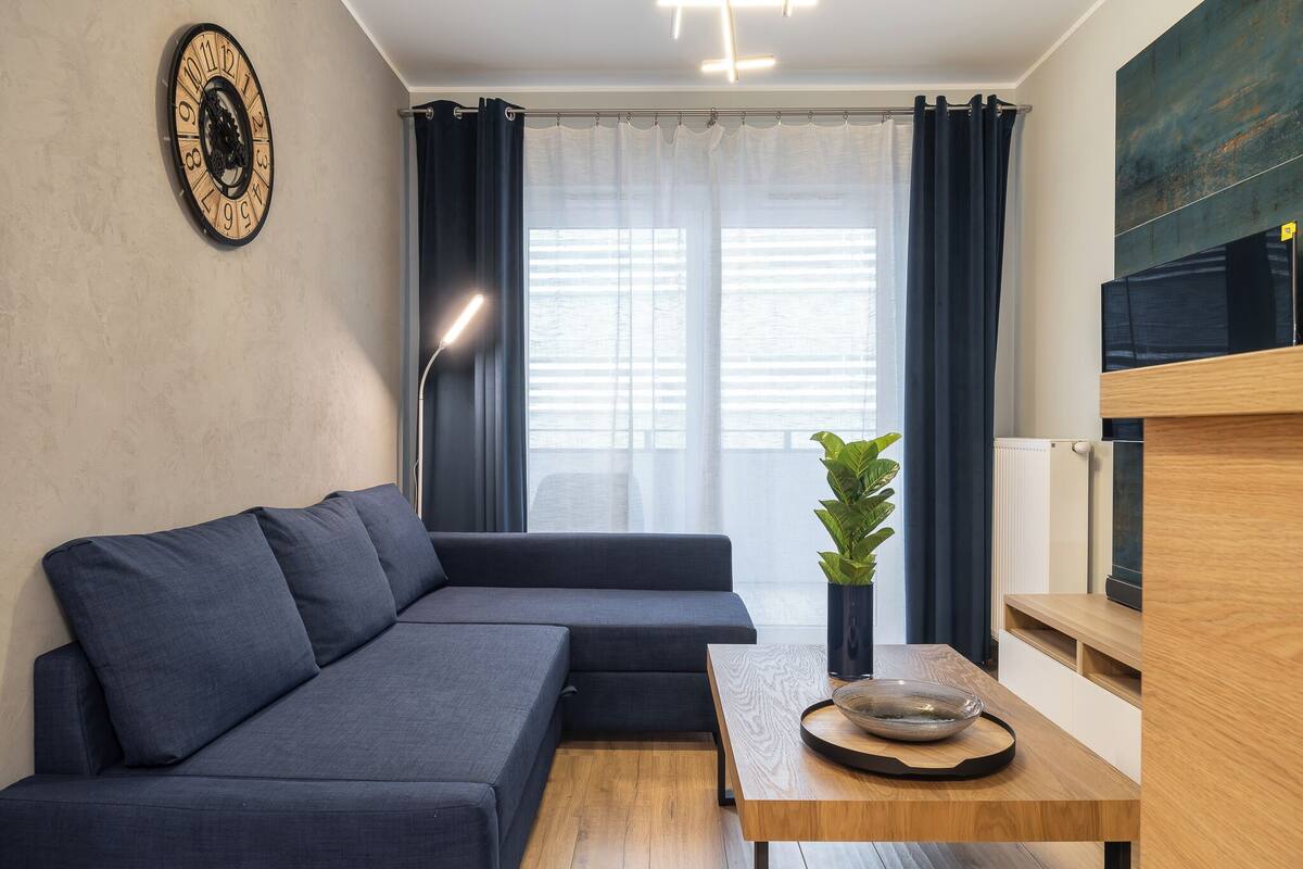 A modern living room with a dark blue sectional sofa, a wooden coffee table, and a potted plant.