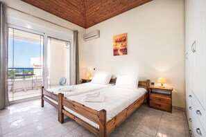 A bedroom with a wooden bed, two bedside tables with lamps, a painting on the wall, and a balcony with a view. - Wonderful Villa with Private Pool, Panoramic Sea Views & Spacious Interiors (Chania)