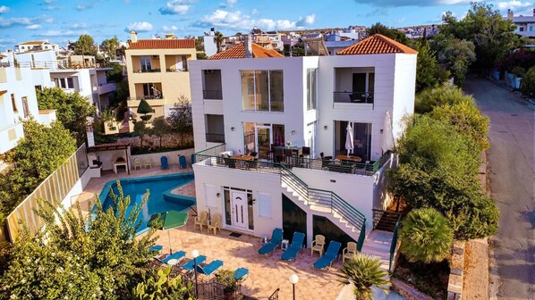A modern two-story building with a swimming pool, outdoor seating, and a view of the surrounding neighborhood. - Wonderful Villa with Private Pool, Panoramic Sea Views & Spacious Interiors (Chania)