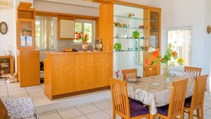Une cuisine moderne avec des meubles en bois, une étagère vitrée et un coin repas comprenant une table et des chaises.