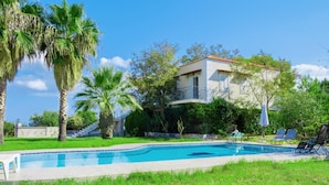 Une piscine avec des chaises longues, une maison dotée d’un balcon et des palmiers.
