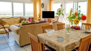 Un salon comprenant un canapé, une table à manger et des chaises. Un téléviseur est fixé au mur, et une horloge est placée au-dessus.
