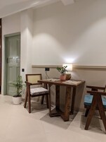 A dining area with a wooden table, two chairs, a potted plant, and a wall-mounted light fixture.