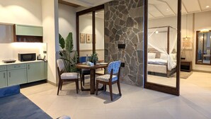 A modern bedroom with a stone accent wall, a canopy bed, and a dining area with a table and chairs. - Cape House at Amritsar (Amritsar)