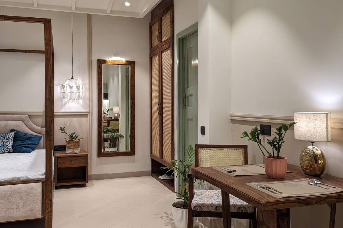 Una habitación de hotel moderna con cama, mesita de noche, espejo y un rincón comedor con mesa y sillas.