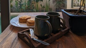 A wooden table with pastries, two mugs, a knife, and a potted plant. - Cape House at Amritsar (Amritsar)
