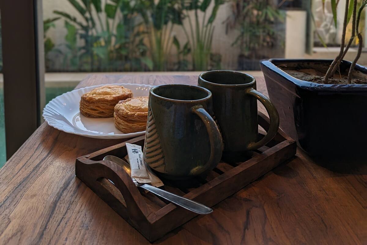 Una mesa de madera con pasteles, dos tazas, un cuchillo y una planta en maceta.