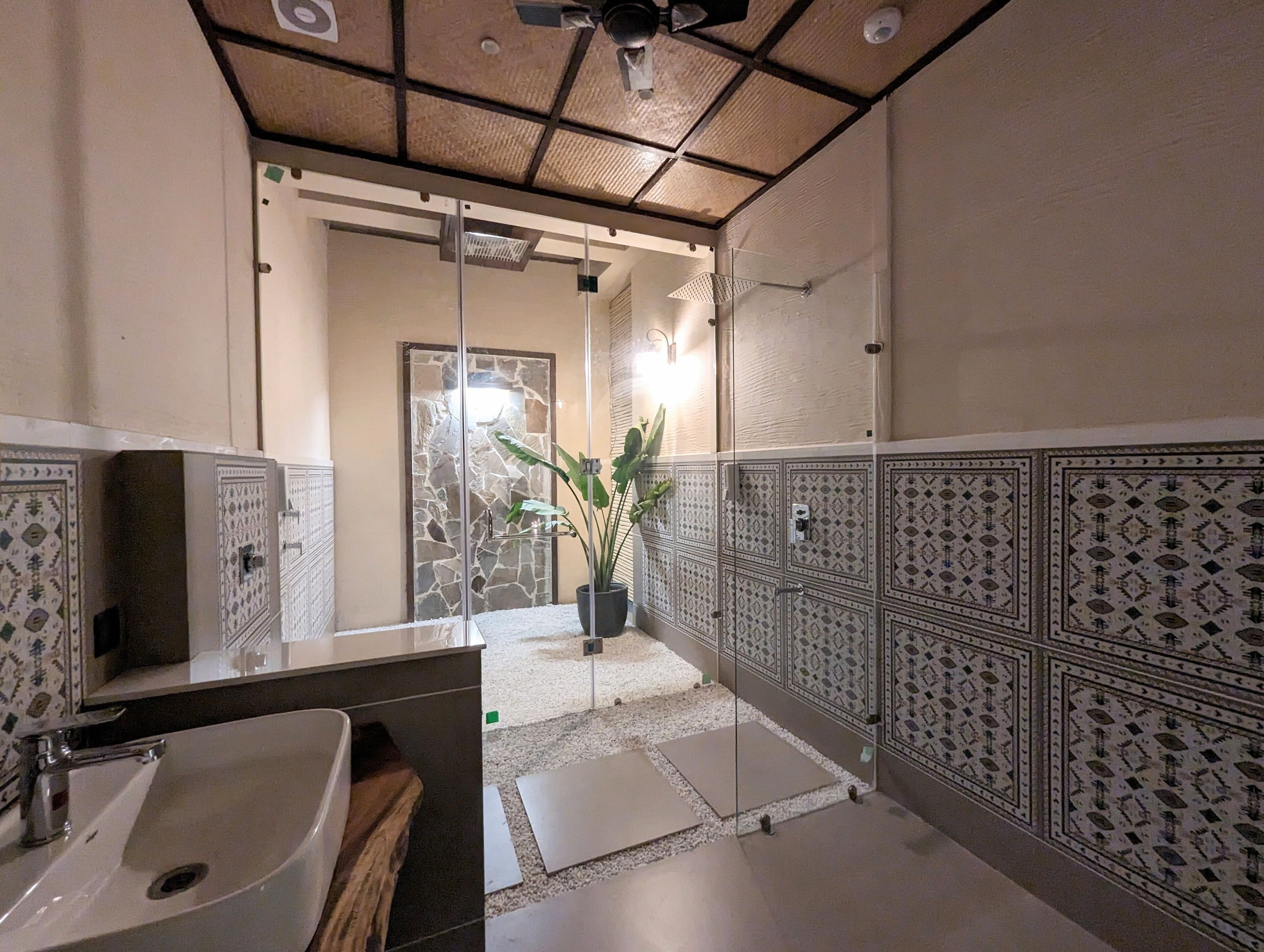 Un bagno con un grande specchio, un lavandino, zona doccia e piastrelle decorate.