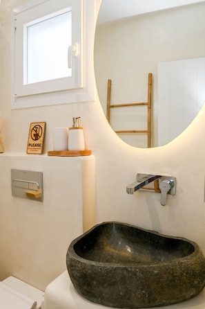 A bathroom with a stone sink, a hand dryer, a towel dispenser, and a "Please do not throw trash here" sign. - Seaclusion (Santorini)