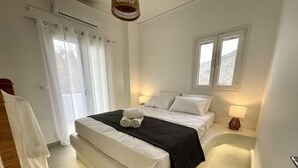 A bedroom with a large bed, a bedside table with a lamp, and a window with a view of the outdoors. - Seaclusion (Santorini)