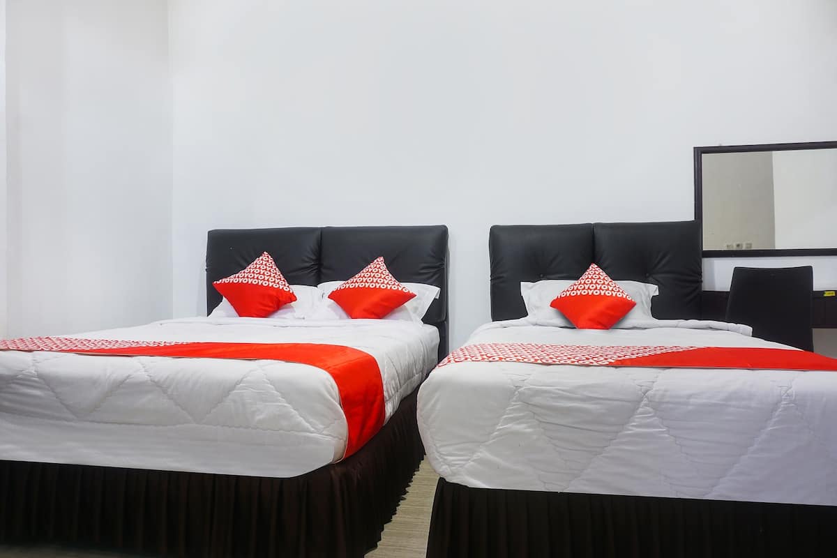 Dos camas individuales con cabeceros negros, ropa de cama blanca y almohadas rojas.